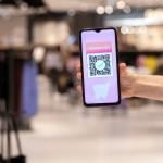 A woman's hand holding a phone displaying promo code applied by scanning a QR code inside a shopping mall.