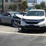 Two modern vehicles involved in a traffic accident are shown stopped in an intersection during the day in Los Angeles.