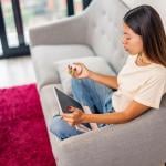 A neurodivergent young woman sitting comfortably on sofa, using digital tablet managing mental health in home environment.