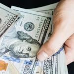 A person's hand counting $100 dollar bills.