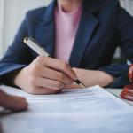 Torso of a female lawyer signing a document for a client in their office.