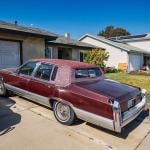 An old red vintage car parked on the driveway of a home.