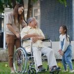 A disabled senior grandfather with his daughter and grandchild in a park.