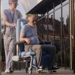 Two doctors assisting a disabled elderly man to the clinic entrance.