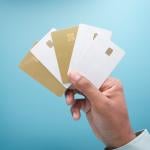 A hand holding an assortment of five gold and white credit card against a blue background.