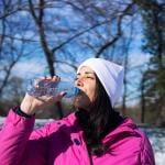 A female athlete in winter clothes drinking water outdoors.