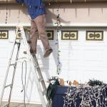 A man on a ladder carefully removes Christmas lights in their home.