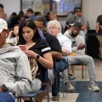 People seated for a queue where most are waiting by being on their phones.