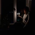 A woman standing by the window holding a candle during a power outage.