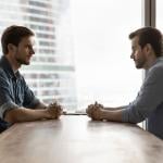 Two businessmen sitting across a table from each other engaged in discussion.