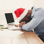 A tired businessman wearing a Christmas hat while asleep at work.