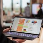 A businessperson holding a laptop that displays data charts and graphs.