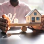 A person balancing figures of a percentage and a small house.