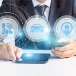 Person wearing business suit and fancy watching with face not showing looking at tablet and smartphone, with icons of cars, 24 hour phone service and agent superimposed symbolizing AI services. 