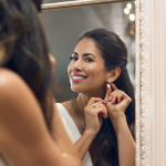 A woman looking at the mirror putting on her earrings.