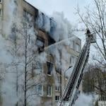 A firefighter on a lift sprays water from a hose into an apartment building as smoke pours out.. 