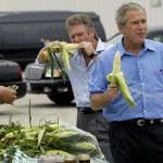 Former US President George W. Bush (R) holding an ear of corn, joined by his friend, Larry Gaitlin (C) while farmer Ken Thompson (L) counts the money handed to him by Bush for a bag of corn, during an impromptu stop of his motorcade at a local farmers market after a campaign rally August 4, 2004 in Davenport, Iowa.