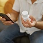 Person holding a prescription medicine bottle and checking info using smartphone.