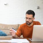 A stressed man reviewing credit card and utility expense documents at home.