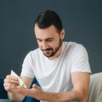 A man squeezing a tube of face cream.
