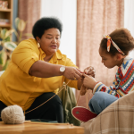 An older woman and a young girl sit in a living room as they wind yarn.
