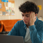 A stressed young adult sitting in front of a laptop. 