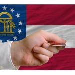 A person's hand holding a credit card with a background of US state Georgia's flag.