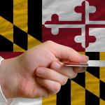 Person's hand holding a credit card with a background of Maryland's flag.