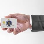 A person's hand holding a credit card designed with the flag of Massachusetts.