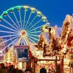 A ferris wheel lights up the night sky during twilight at the Erfurt Christmas Market with vendors selling festive goods in the foreground.