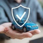Person holding a small figure of a car illustrated with a shield as a concept of car insurance.