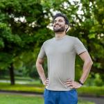 A sporty young man standing outdoors with hands on hips, smiling after an exercise.