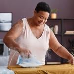A senior woman happily ironing clothes at home.