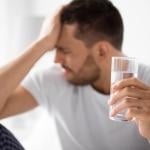 Man experiencing hangover holding a glass of water.