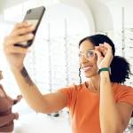 A young woman trying on eyeglasses in a shop and taking a selfie.