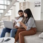A couple sitting together on a sofa and reviewing bills.
