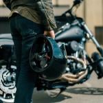 Close up of person holding motorcycle helmet with Harley type motorcycle in the background.