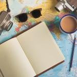 Traveller items such as a camera, sunglasses, and an empty planner on top of a world map.