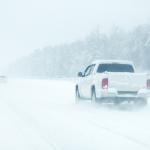 Rear view of a white pickup truck on the road during heavy snowfall.
