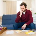 A worried man calculating expenses at home.
