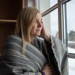 Woman wrapped in blanket looking out the window during winter.