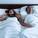 A couple sleeping in bed together where the wife is disturbed by her husband's snoring.