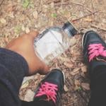 A selfie-style photo showing a person holding a water bottle and their fitness shoes while outdoors.
