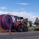 Machinery vehicles parked on roadside while installing internet fiber optic cables' plastic conduit underground in a rural area in Utah.
