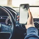 Person's hand holding up a smartphone while driving.