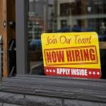 A 'now hiring' sign displayed on a glass window.