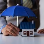A figure of a house with a person holding small umbrella over it as a concept of home insurance.