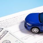 A small figure of a blue car on top of banknotes and insurance documents.