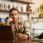 Man glumly staring at his laptop in a coffee shop.