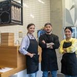 A team of young cafe workers pose in front of their shop's front bar.